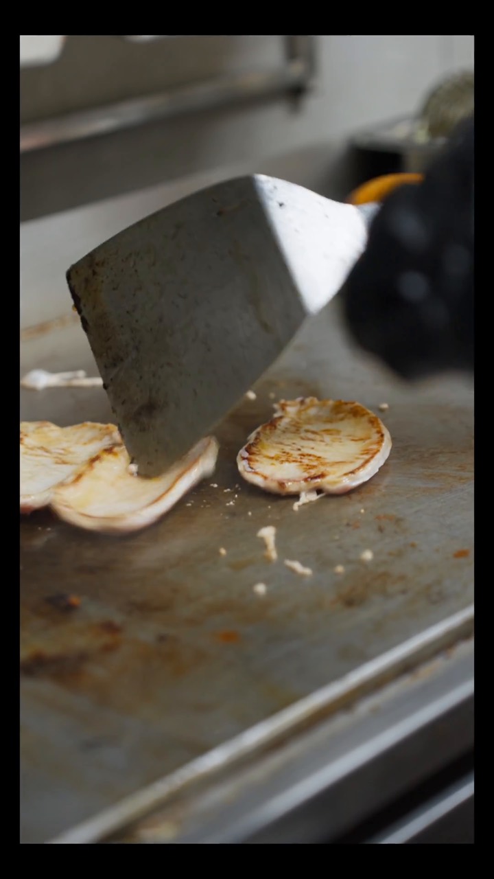 Espátula y pan de hamburguesa tostándose en la plancha
